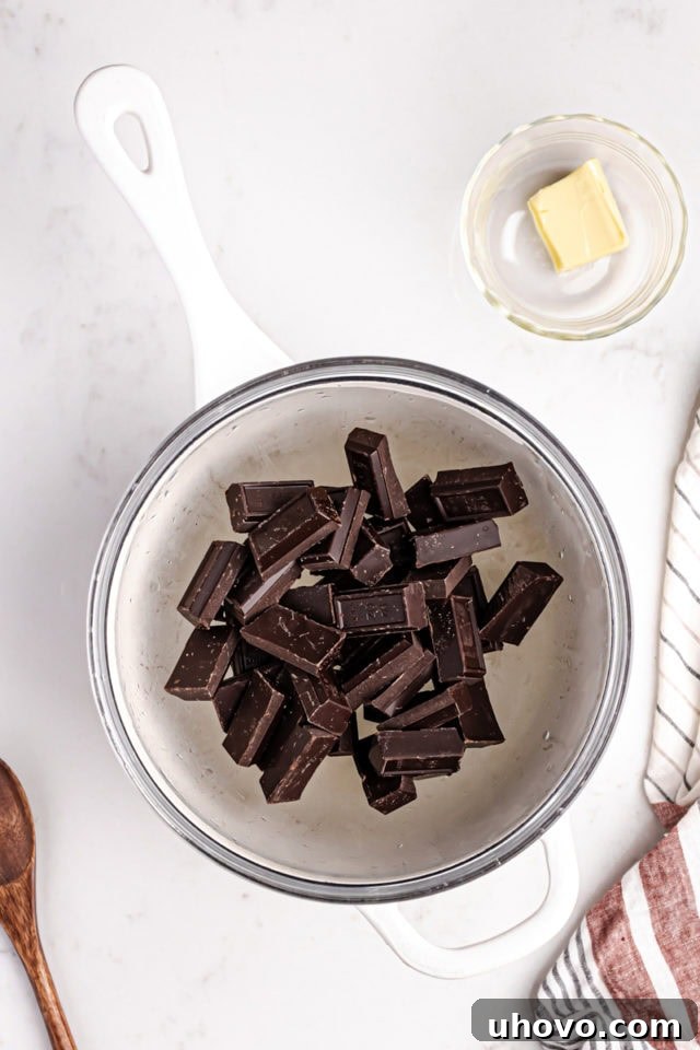 Chopped semisweet chocolate melting in a heatproof bowl set over a pot of simmering water (double boiler method) for a perfectly smooth chocolate topping.
