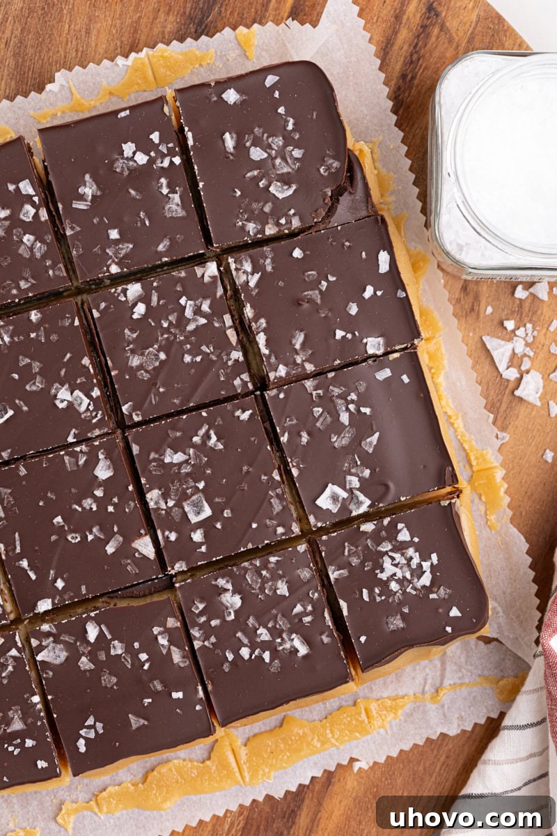 An overhead shot of a batch of Millionaire Shortbread Bars, perfectly cut into uniform squares, arranged on a wooden cutting board with parchment paper, ready to be served.