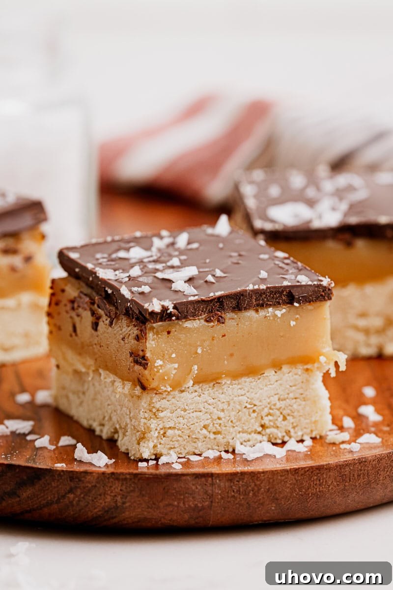 A perfectly cut Millionaire Shortbread Bar sitting on a wooden cutting board, highlighting its distinct layers and appealing texture, ready for serving.