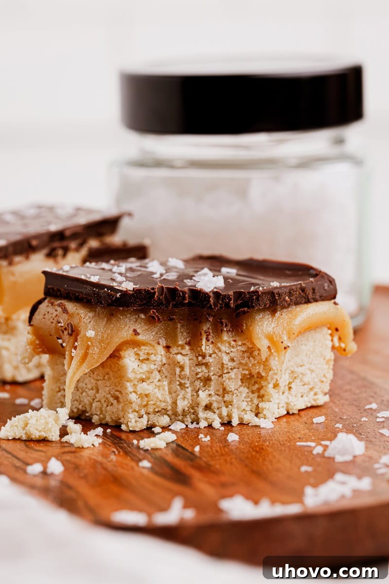 A Millionaire Shortbread Bar with a bite taken out of it, showcasing the distinct shortbread, caramel, and chocolate layers, emphasizing its deliciousness.