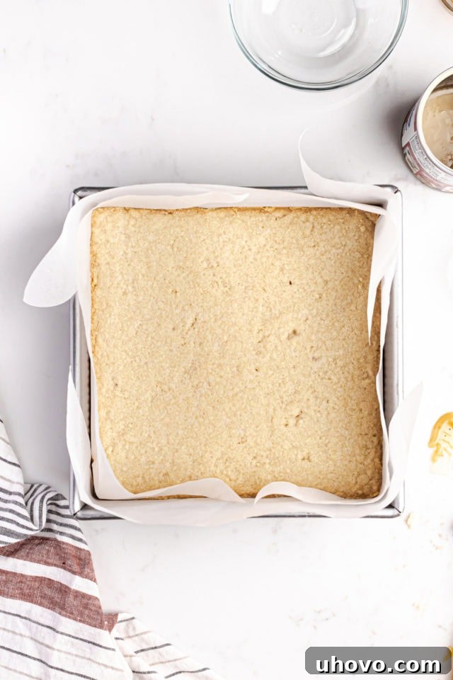 Freshly baked shortbread base, golden brown around the edges and perfectly set, resting in a square baking pan after coming out of the oven.