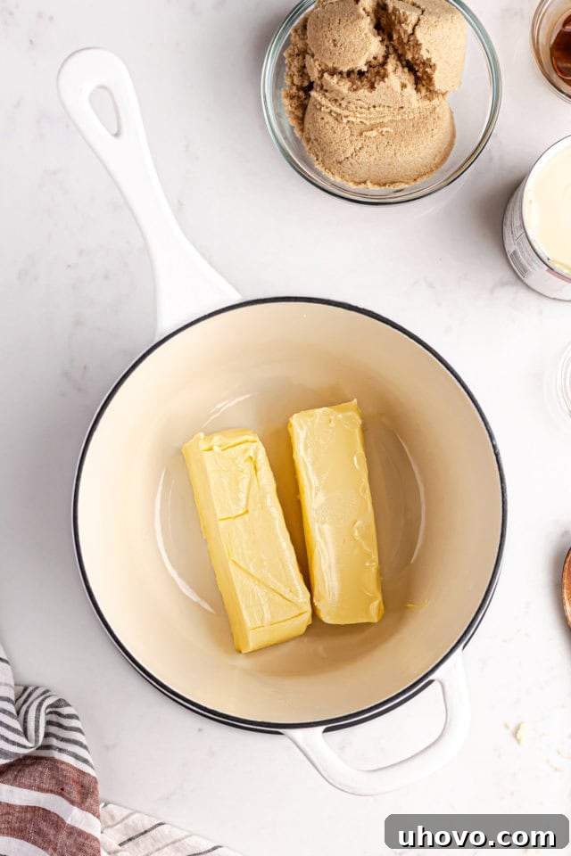 Close-up overhead view of unsalted butter melting in a medium saucepan over gentle heat, preparing for the caramel layer.