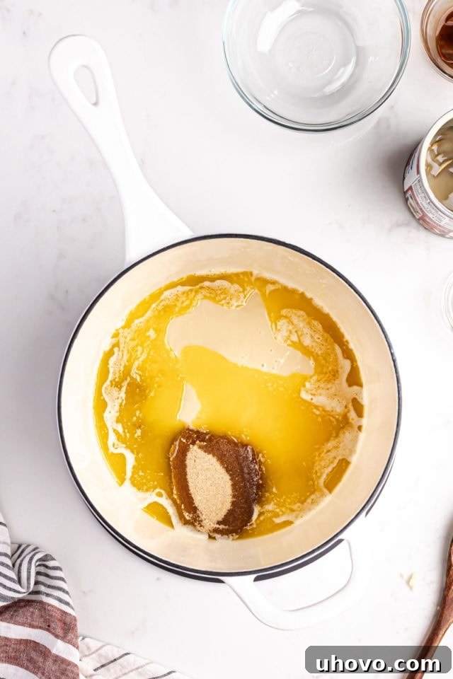 Overhead view of brown sugar, sweetened condensed milk, and corn syrup being added to the melted butter in a saucepan, ready to be stirred for the caramel layer.