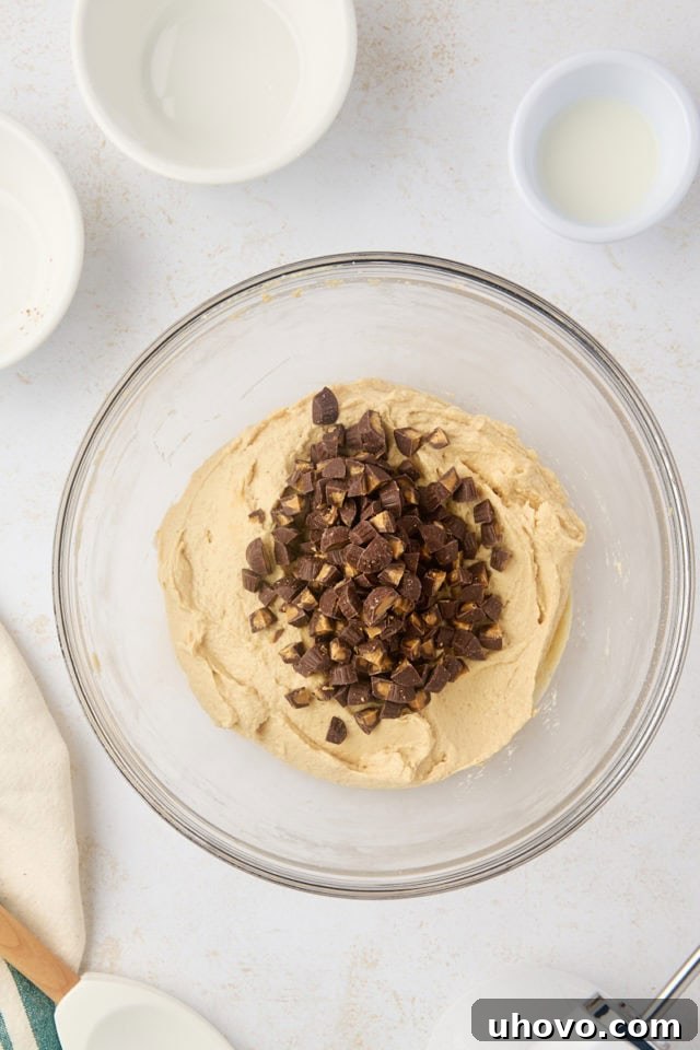 Chopped peanut butter cups gently folded into the creamy peanut butter dip base in a mixing bowl, ensuring even distribution of the delicious chocolate and peanut butter candy.