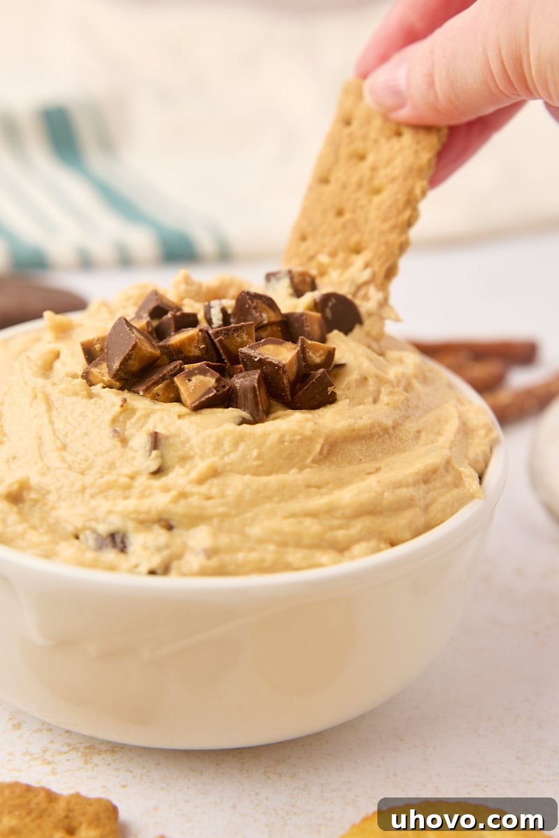 A hand dipping a crispy graham cracker into the rich and creamy peanut butter cup dip, showcasing its perfect consistency for scooping.