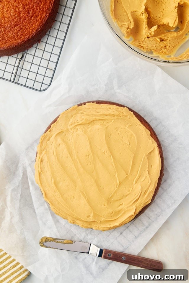 An overhead view of a single cooled cake layer expertly frosted with creamy dulce de leche frosting, demonstrating the first step in assembling the layer cake.