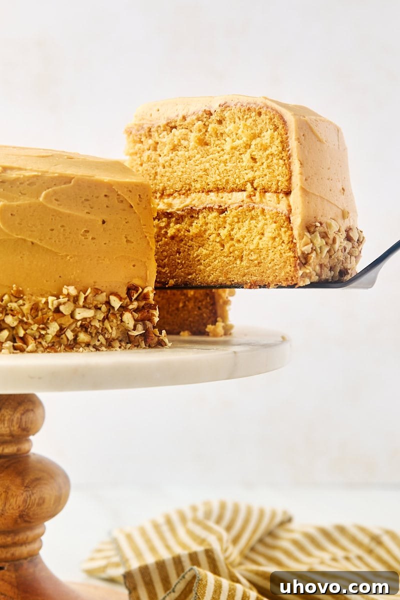 A slice of dulce de leche cake being carefully lifted from the main cake with a cake server, highlighting the soft layers and generous frosting.