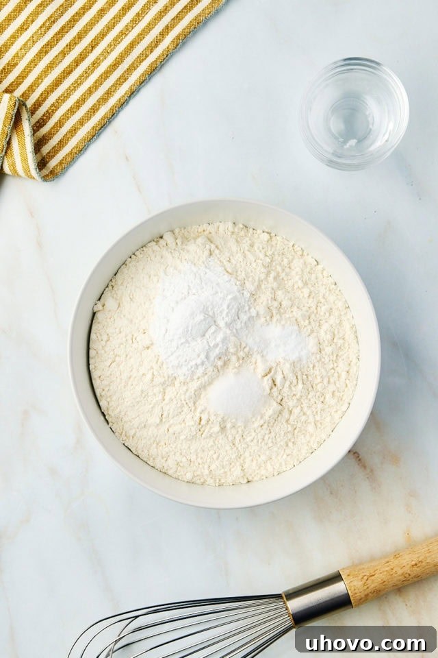 An overhead shot of dry ingredients – flour, baking powder, baking soda, and salt – meticulously measured and combined in a pristine white mixing bowl.