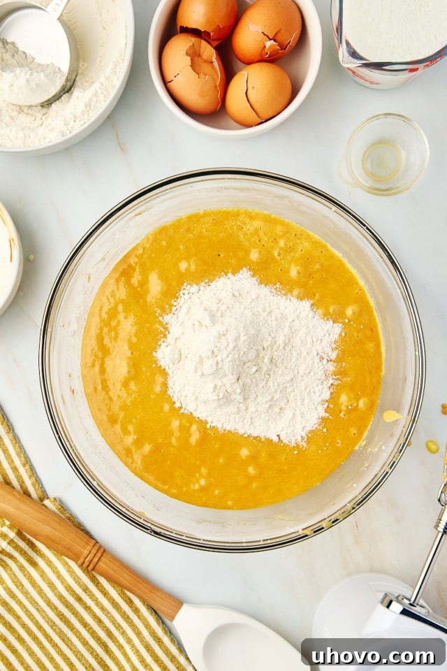 An overhead shot of a portion of dry ingredients being added to the wet ingredients in a mixing bowl for the dulce de leche cake, demonstrating the alternating addition method.