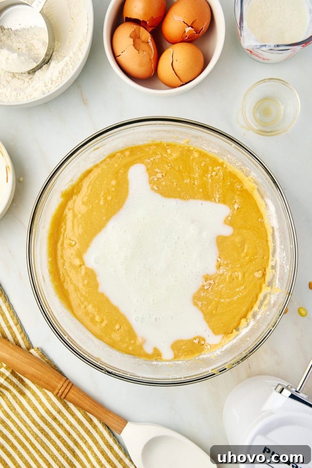 An overhead shot of buttermilk being poured into the dulce de leche cake batter, illustrating the alternating addition with dry ingredients.
