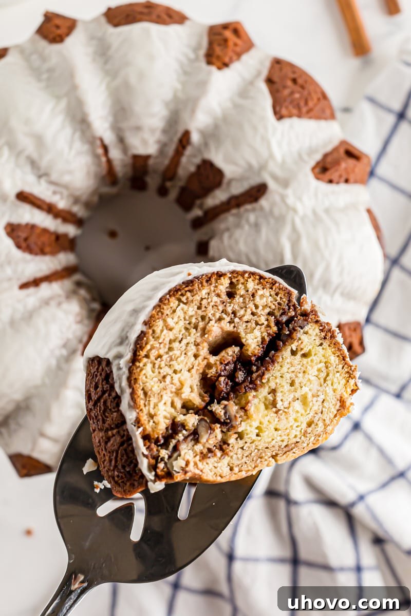 A tempting slice of Cinnamon Roll Cake elegantly lifted on a pie server, with the rest of the beautifully glazed cake blurring in the background.