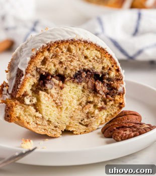 A tempting slice of Cinnamon Roll Cake standing upright on a plate, garnished with two pecans, highlighting its moist texture and rich filling.