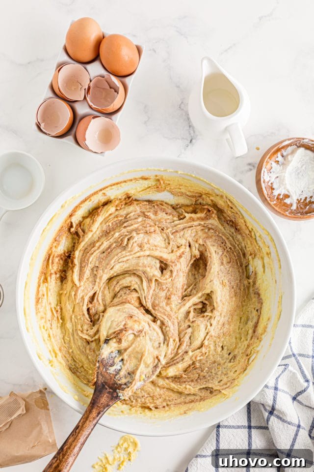 A wooden spoon gently folds a cinnamon and sugar mixture into the prepared cake batter, creating luscious swirls.