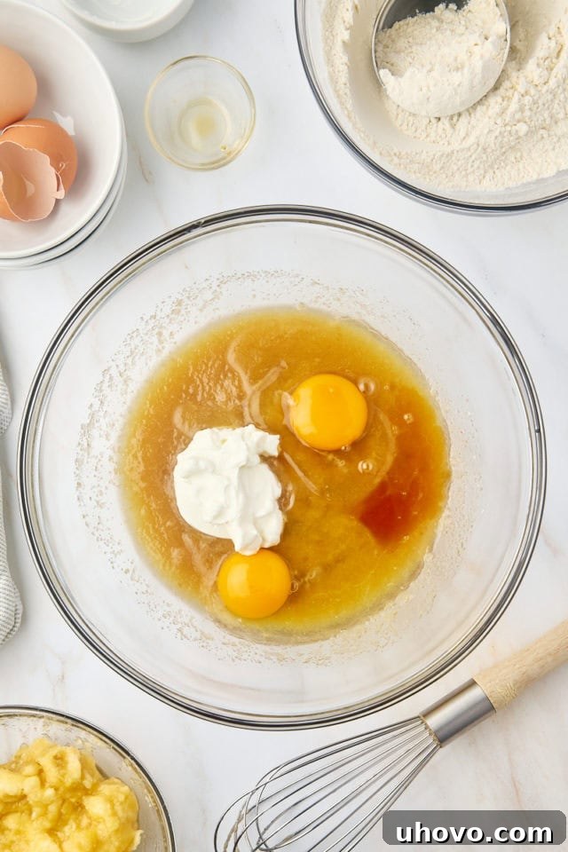 overhead view of eggs, yogurt, and vanilla extract added to banana bread batter