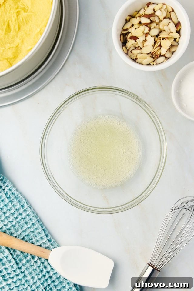 Overhead view of a whisked egg white in a clear glass bowl, appearing frothy and light, ready for the topping mixture.