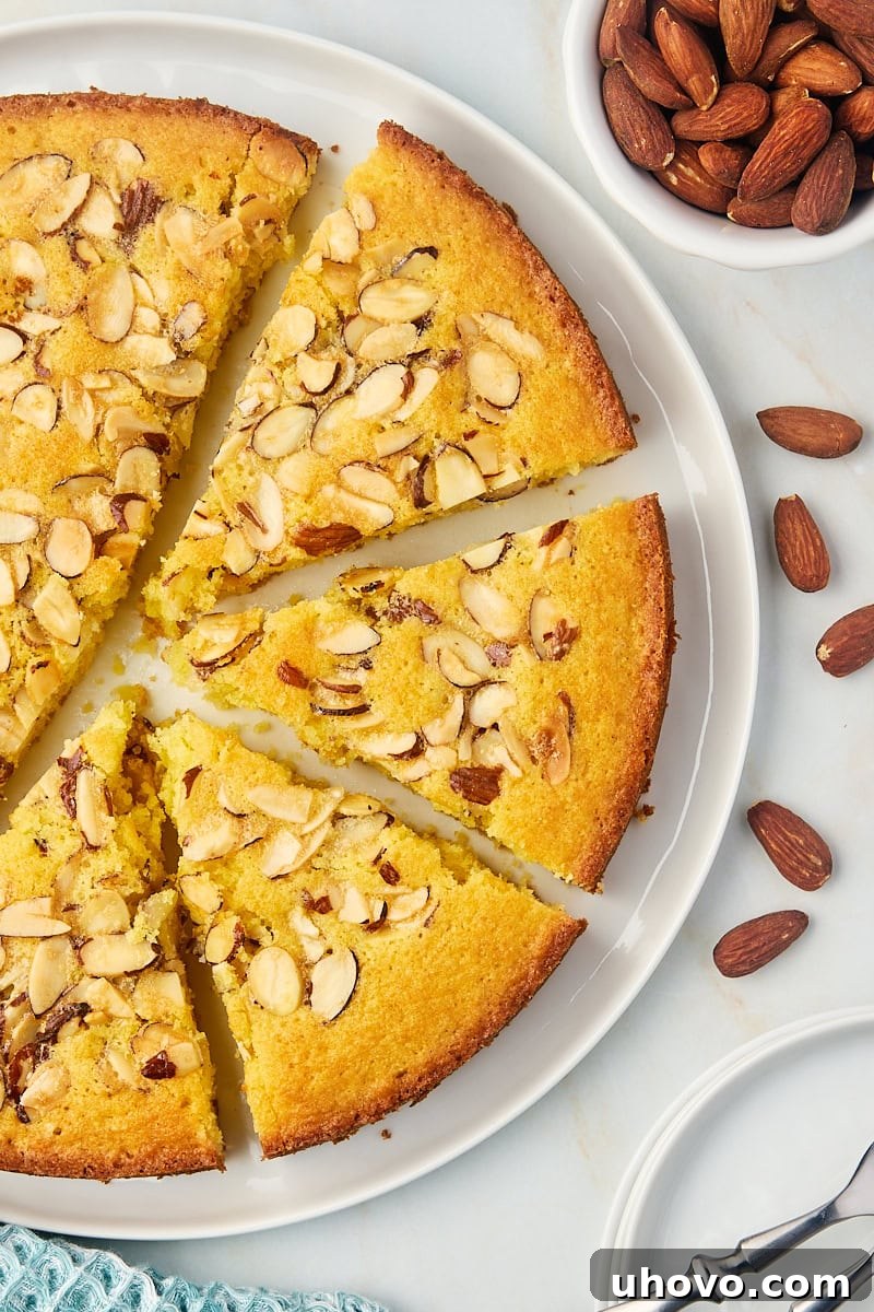 Overhead view of a beautiful almond torte, partially sliced, presented on a pristine white cake plate, ready to be served and enjoyed.