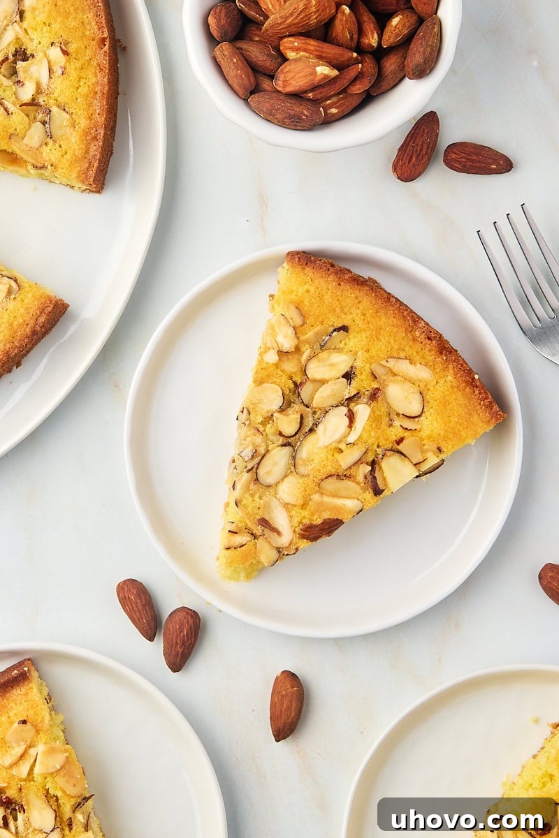 Overhead view of a single slice of almond torte artfully placed on a white plate, with the rest of the torte positioned behind it, highlighting its inviting texture and golden topping.
