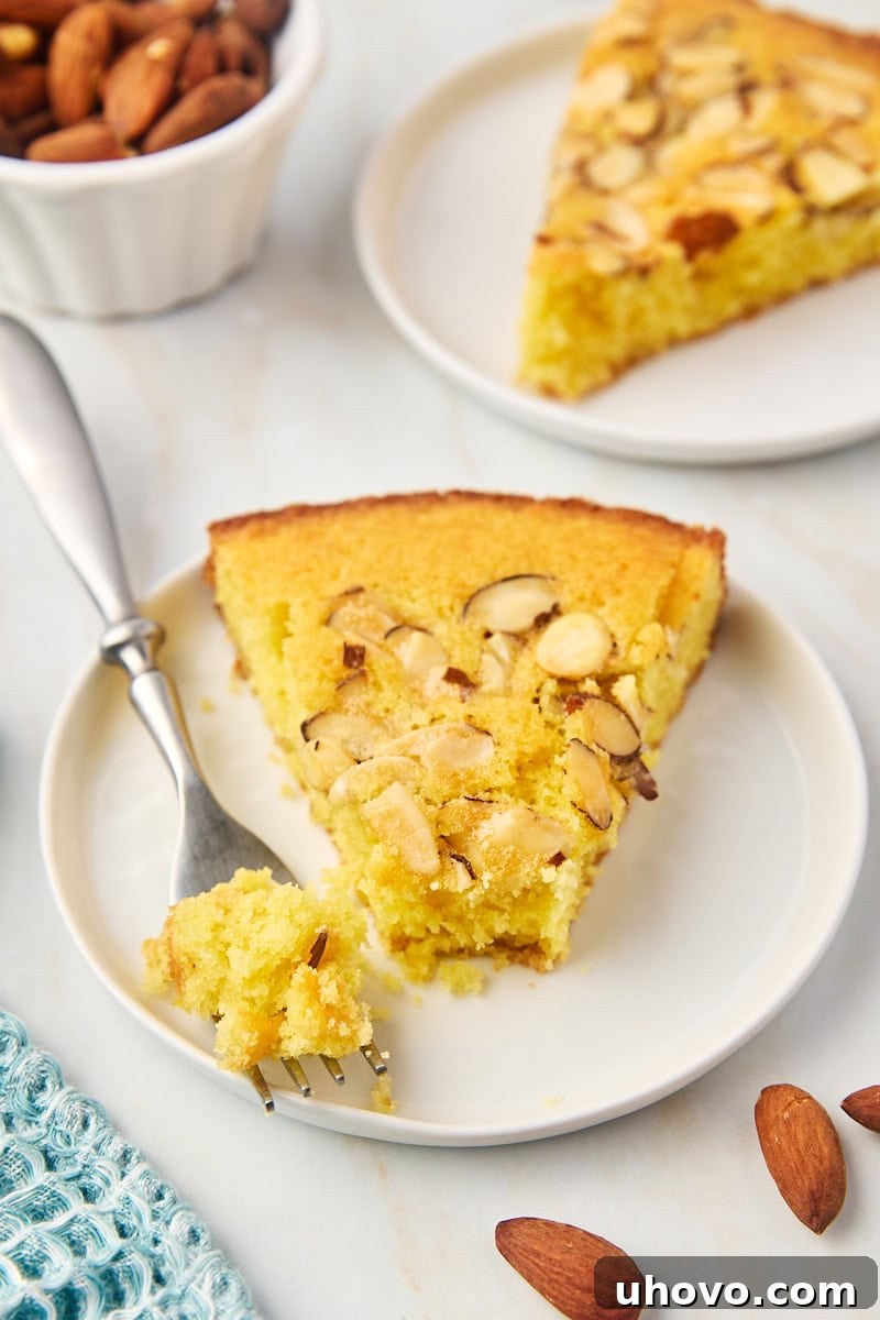 A close-up view of a slice of almond torte on a white plate, with a fork holding a bite-sized piece, highlighting the tender crumb and crunchy topping.