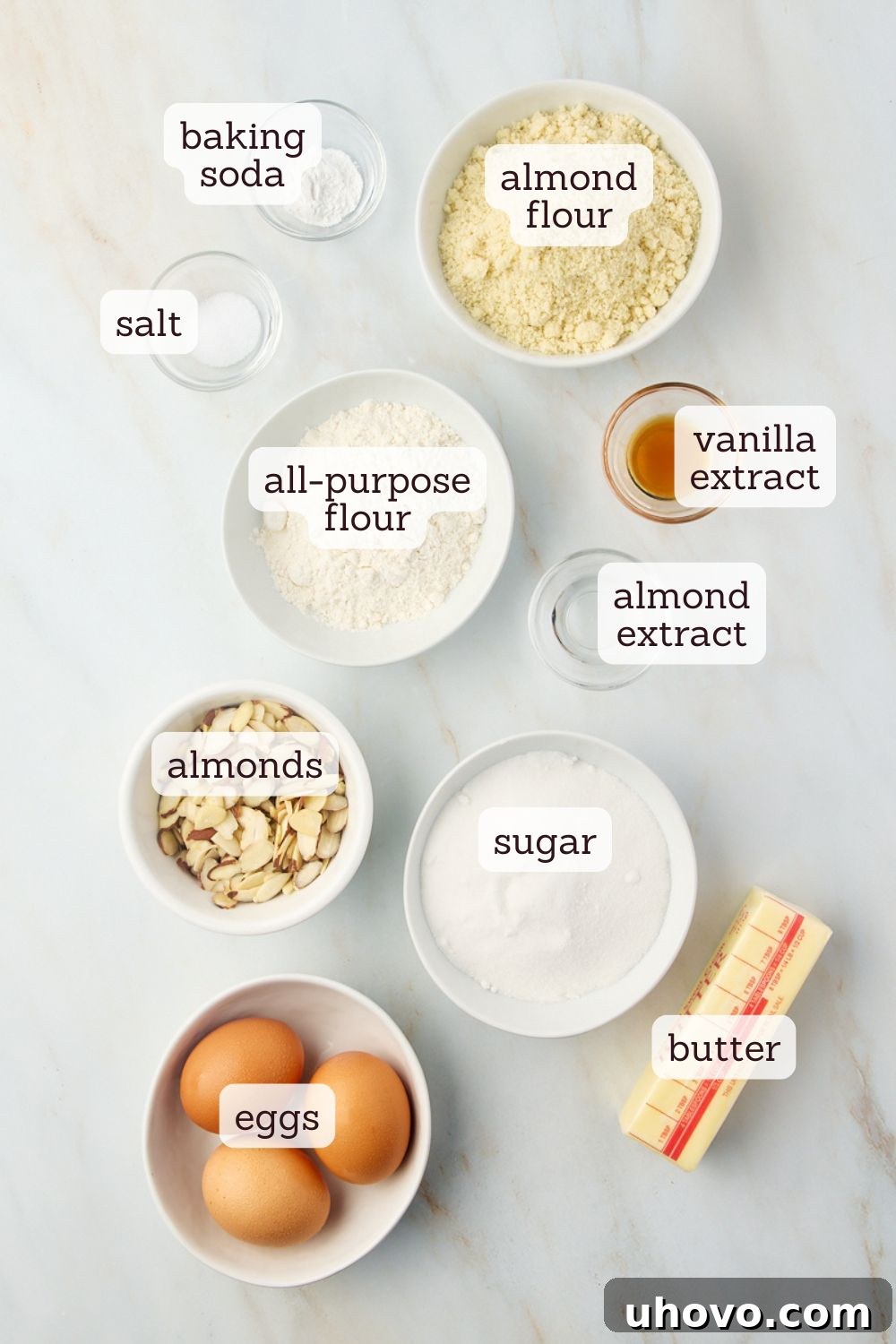 Overhead view of various almond torte ingredients neatly arranged on a counter, including flours, butter, eggs, and extracts.