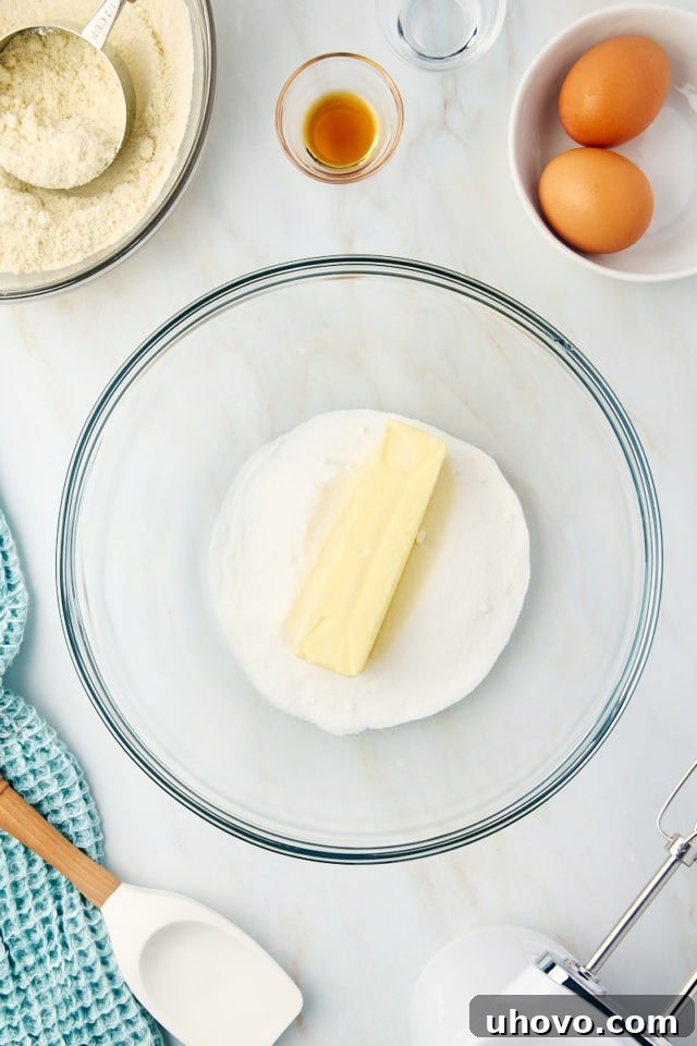 Overhead view of softened unsalted butter and granulated sugar being creamed together in a glass mixing bowl, appearing light and fluffy.
