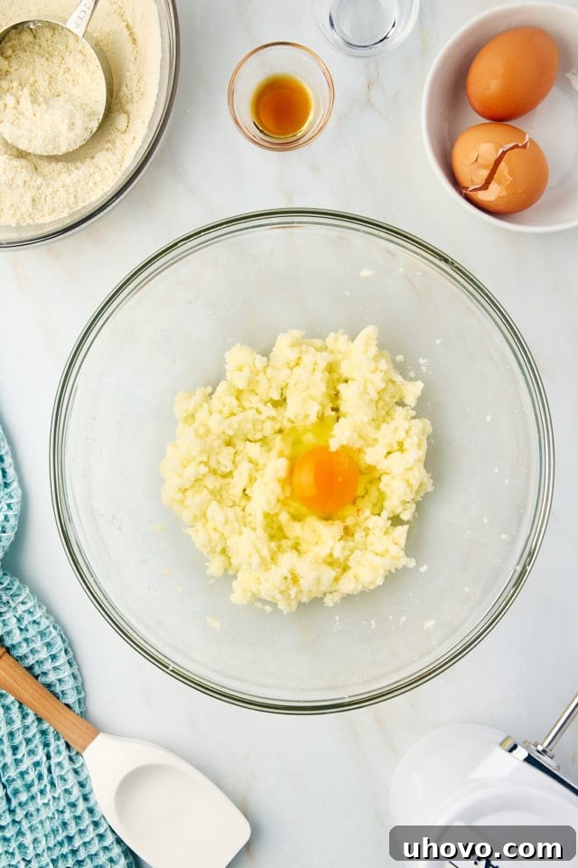 Close-up overhead shot of a single egg being gently incorporated into the creamed butter and sugar mixture in a glass bowl.