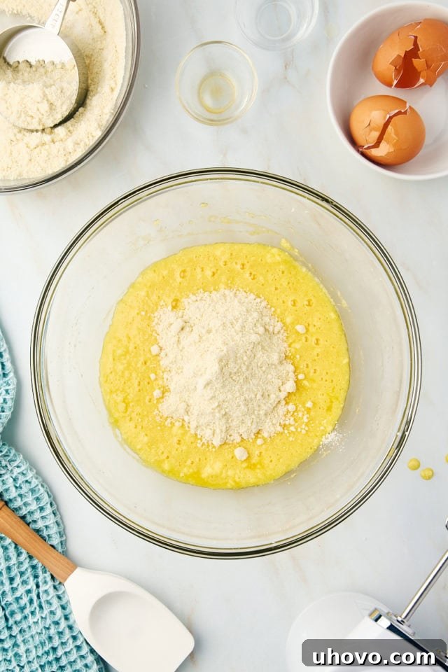 Overhead view of the dry flour mixture being gradually added to the wet ingredients in a large mixing bowl for the almond torte.