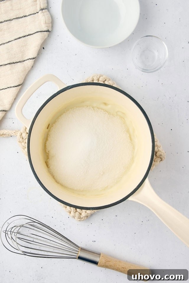 Overhead view of granulated sugar and salt being added to the hot, thickened milk mixture for the ermine frosting, just removed from heat.