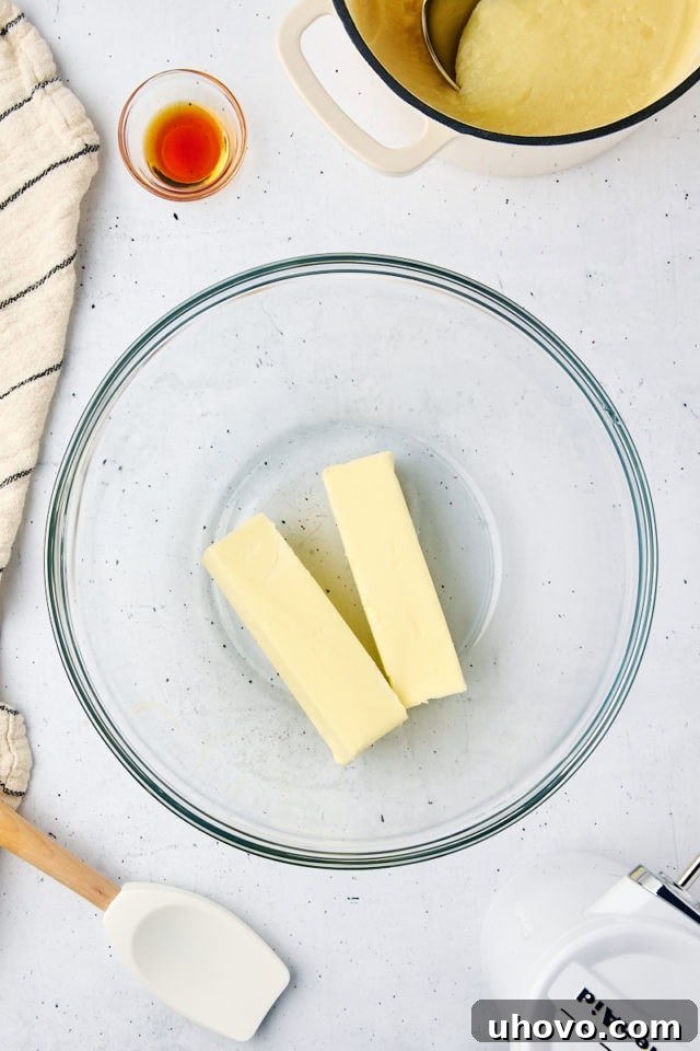 Overhead view of softened butter being beaten until light and fluffy in a glass mixing bowl with an electric mixer.