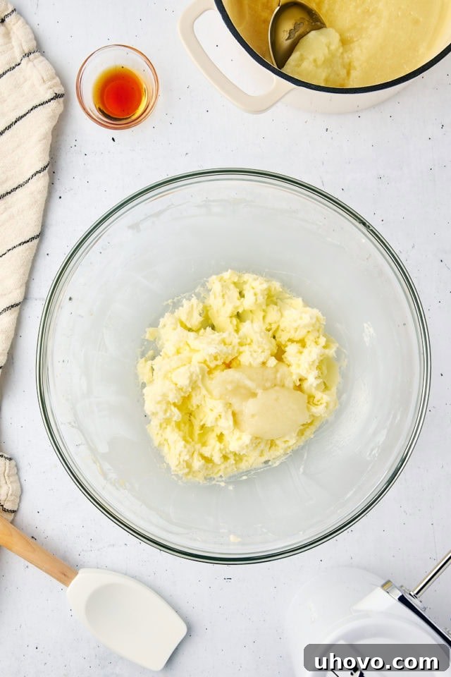 Overhead view of the cooled milk mixture being added in small portions to the beaten butter for ermine frosting, ensuring smooth incorporation.