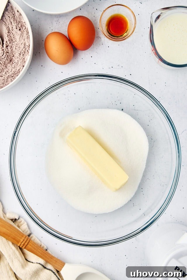Overhead view of softened butter and granulated sugar being creamed together in a clear glass mixing bowl.