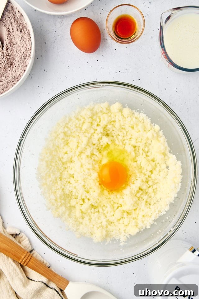 Overhead view of a cracked egg added to the creamed butter and sugar mixture in a glass bowl.
