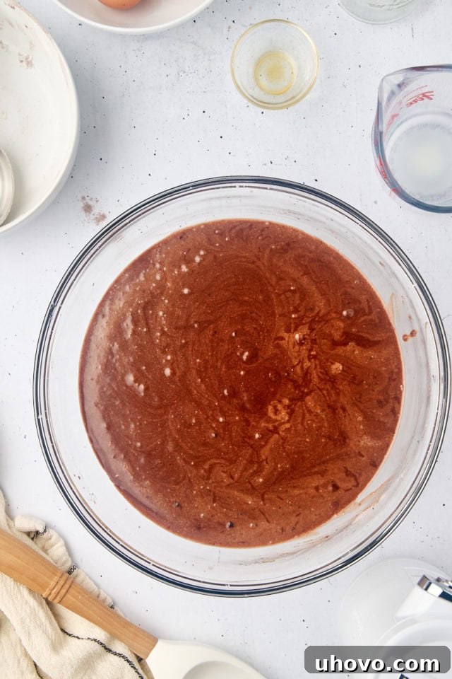 Overhead view of the fully mixed mahogany cake batter, smooth and reddish-brown, in a clear glass mixing bowl.