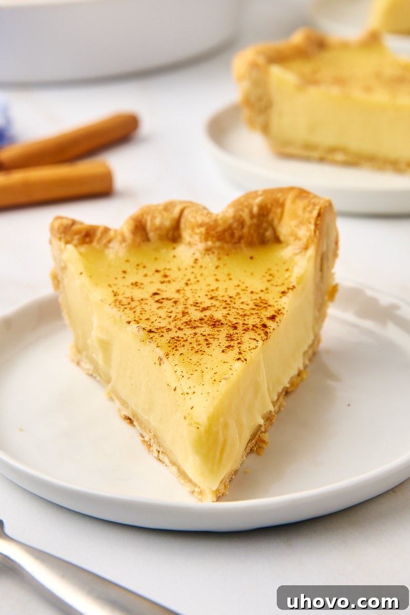 A perfectly sliced sugar cream pie on a white plate, with the rest of the pie in the background, inviting a delicious dessert experience.