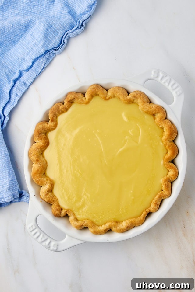 An overhead view of the creamy sugar cream pie filling being carefully poured into a pre-baked pie crust in a white pie plate.