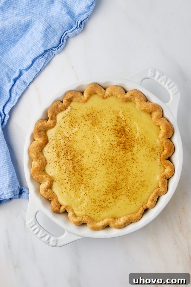 An overhead shot of an assembled sugar cream pie, lightly dusted with cinnamon, ready for its final short bake.