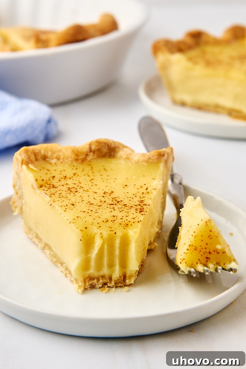 A close-up shot of a slice of sugar cream pie on a white plate, with a fork holding a perfect bite, emphasizing its creamy texture.