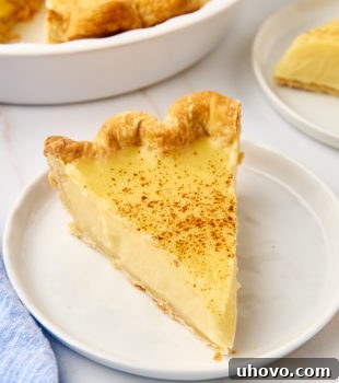 A slice of sugar cream pie on a white plate next to the remaining pie, highlighting its creamy texture.