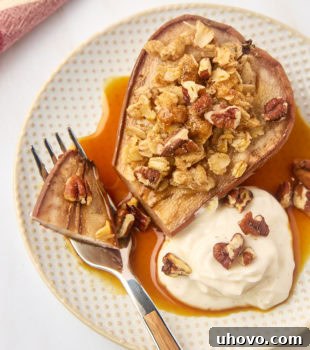 A close-up of a baked pear on a plate with a bite on a fork, highlighting its tender texture and golden topping.