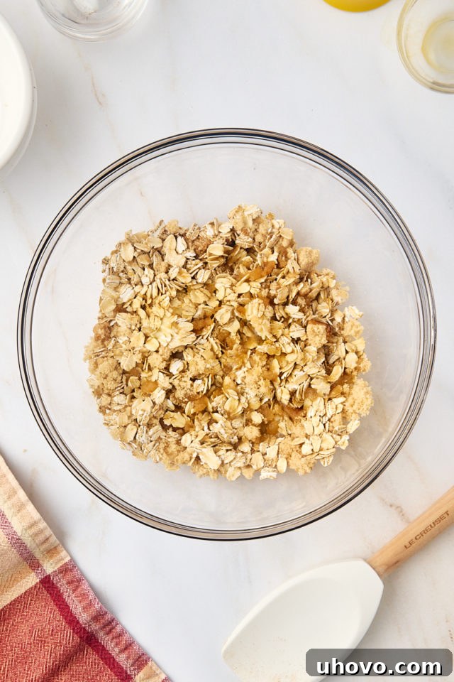 An overhead shot depicting melted butter and fragrant vanilla extract being poured into the dry oat mixture within a mixing bowl, prior to combining.