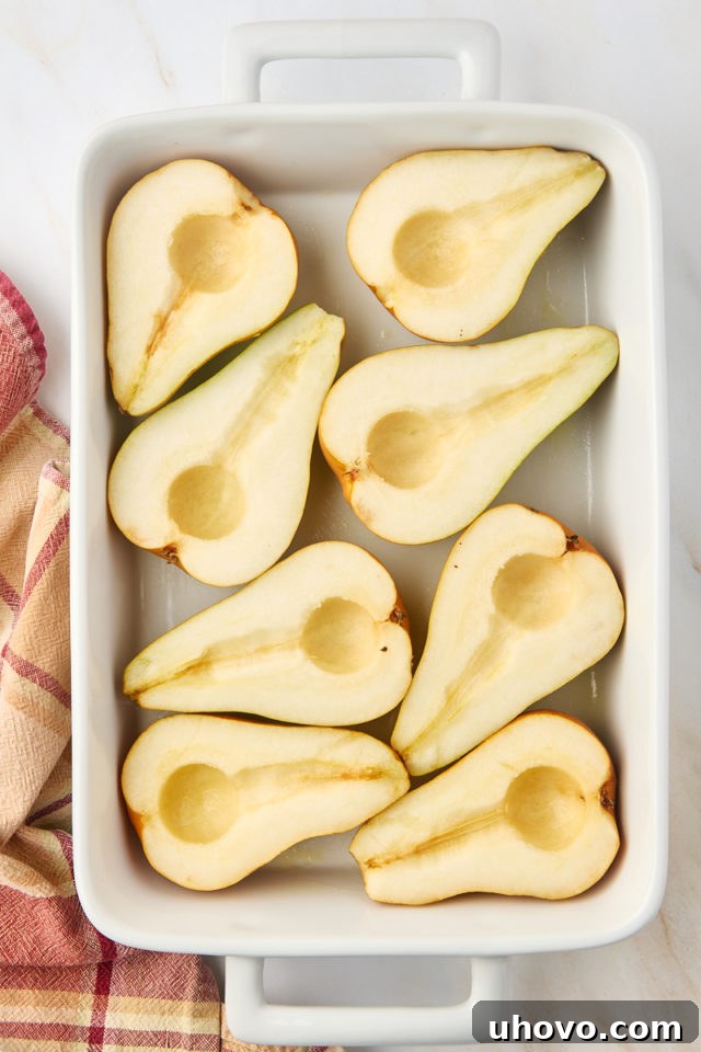 An overhead shot displaying perfectly halved and cored pears arranged neatly in a white baking dish, prepared for filling.