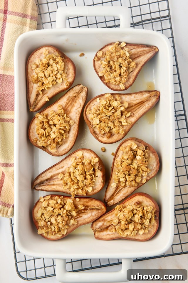 A beautiful overhead view of freshly baked pears, golden and tender, still resting in their white baking dish on a wire rack to cool slightly.