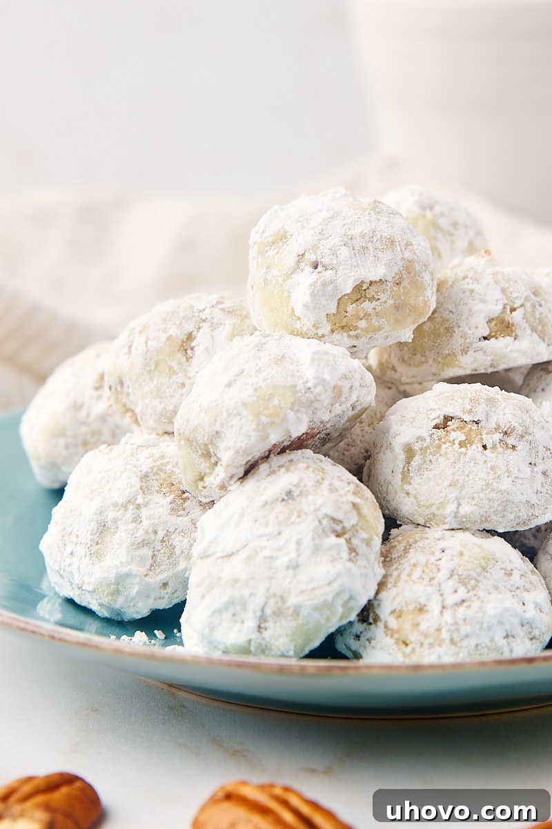 A charming stack of freshly baked snowball cookies on a rustic blue-green plate, showcasing their pristine powdered sugar coating.