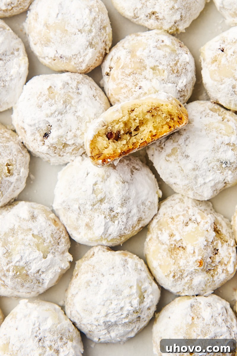 An inviting display of classic snowball cookies on parchment paper, with a cross-section of one cookie revealing its tender, nutty interior.