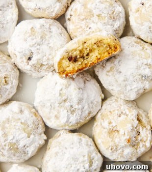 An inviting display of classic snowball cookies on parchment paper, with a cross-section of one cookie revealing its tender, nutty interior.