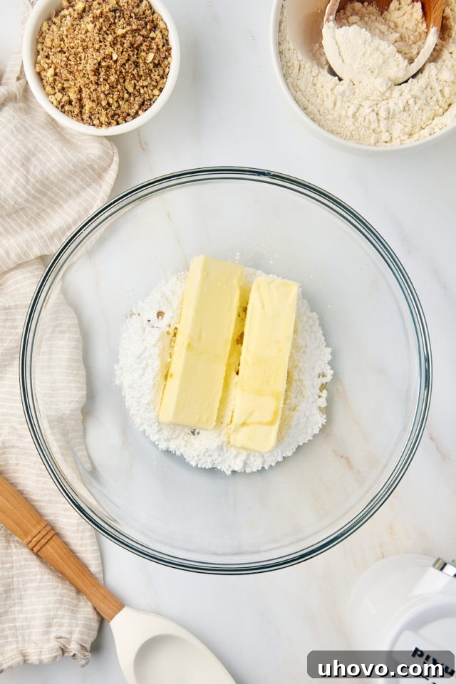 Softened butter, confectioners' sugar, and extracts being creamed together in a glass mixing bowl with an electric mixer.