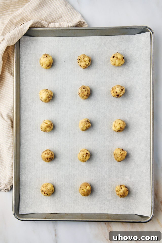 Portioned snowball cookie dough balls neatly arranged on a parchment-lined baking sheet, ready for the oven.