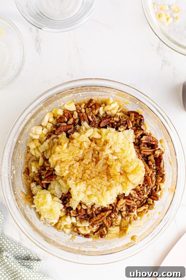 Overhead view of chopped pineapple, banana, and pecans being added to the mixed cupcake batter in a large bowl.