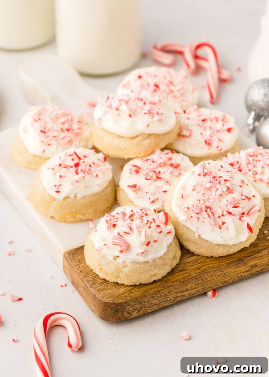 Soft, festive peppermint meltaway cookies on a wood and marble board, topped with creamy frosting and crushed candy canes.