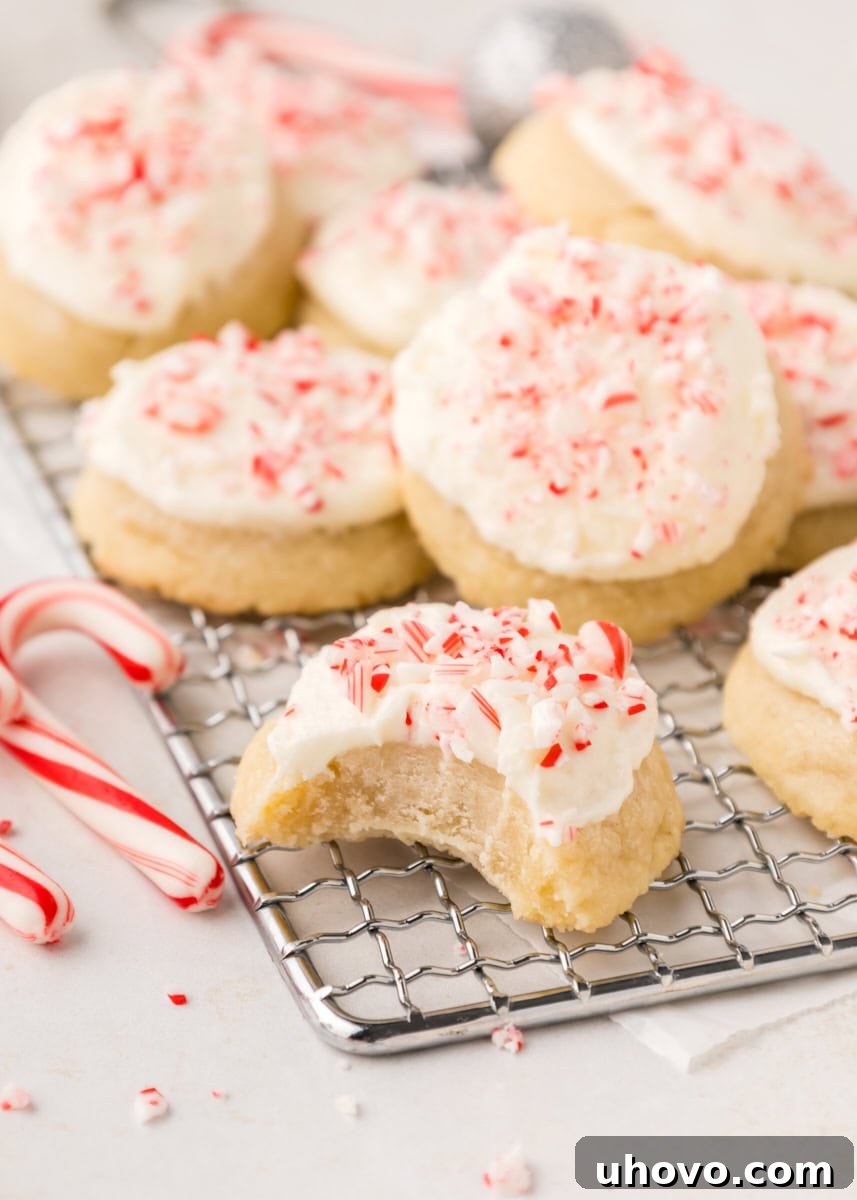 A peppermint meltaway cookie on a wire rack with a small bite taken out of it, revealing its soft interior, with other cookies blurred in the background.