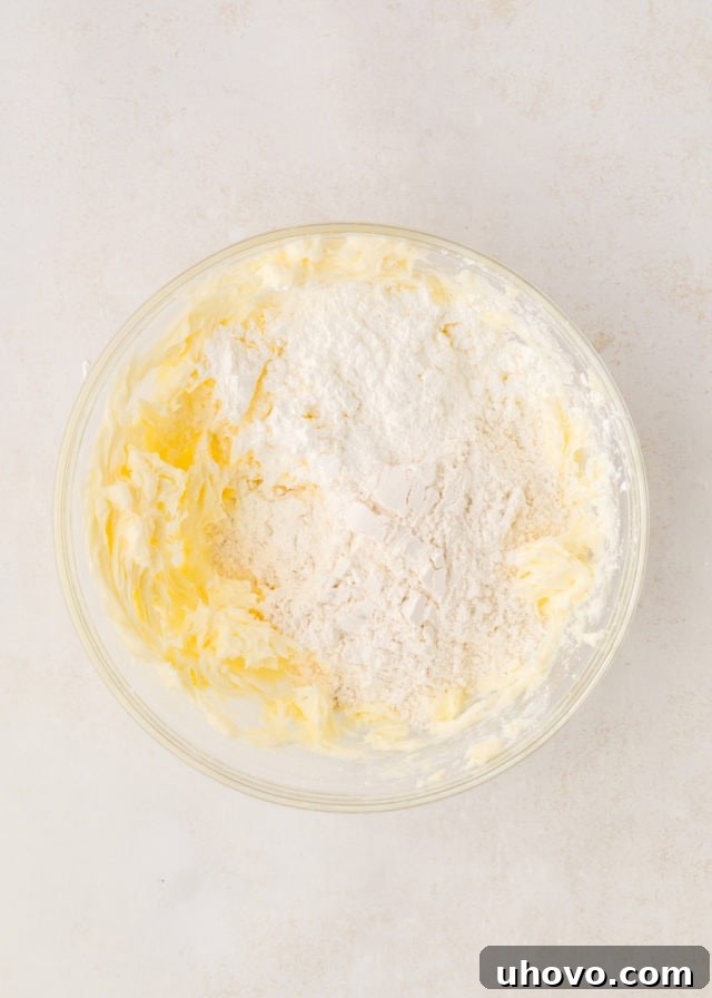 Overhead view of all-purpose flour and cornstarch being added to the creamed butter and sugar mixture.
